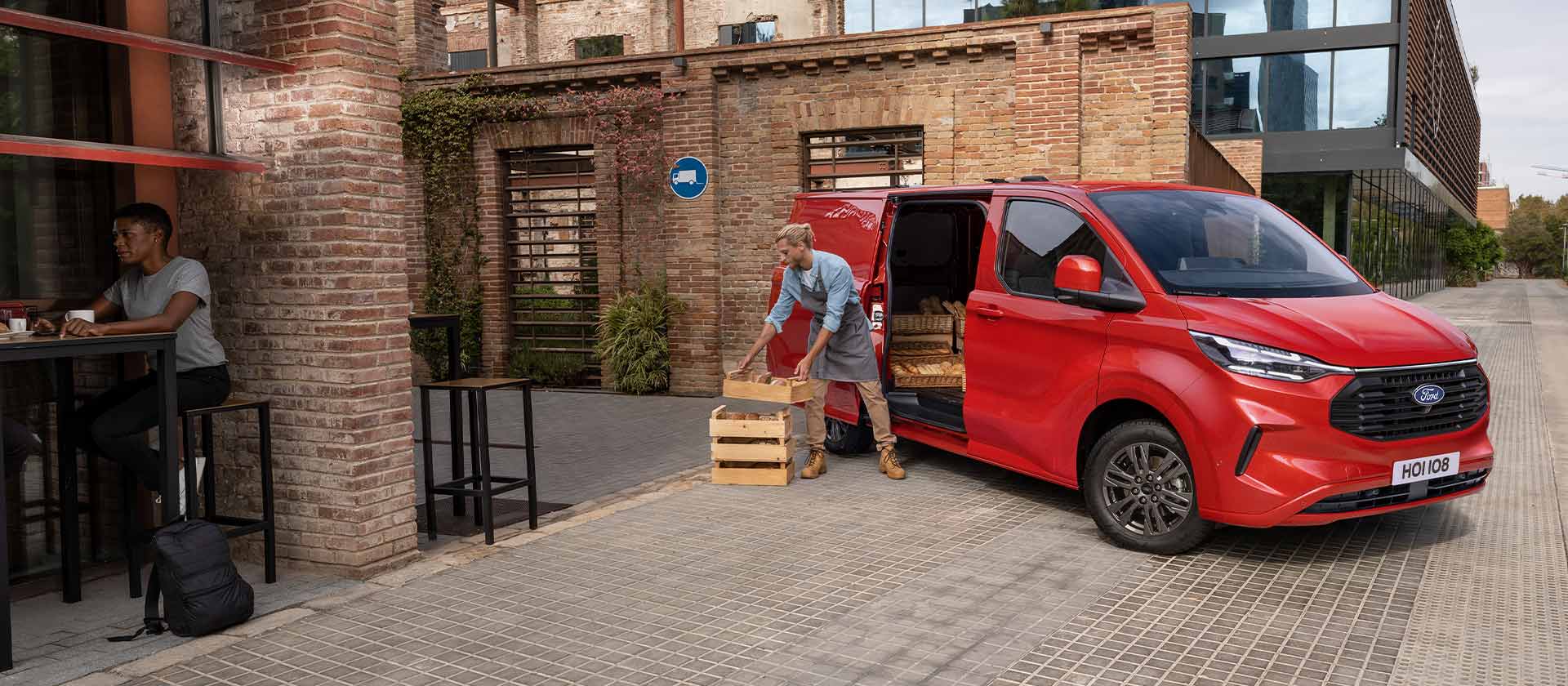 Egy piros Ford Transit Custom egy kávézó előtt parkol.