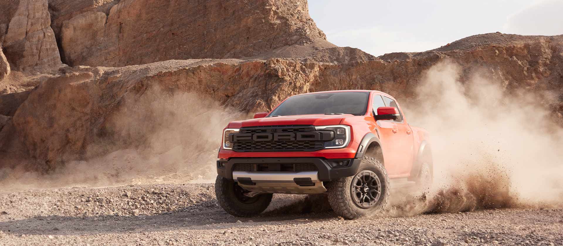 Egy Code Orange színű Ford Ranger Raptor zúzott köves terepen halad.