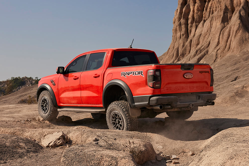 Egy Code Orange színű Ford Ranger Raptor sziklás terepen halad hegymenetben.
