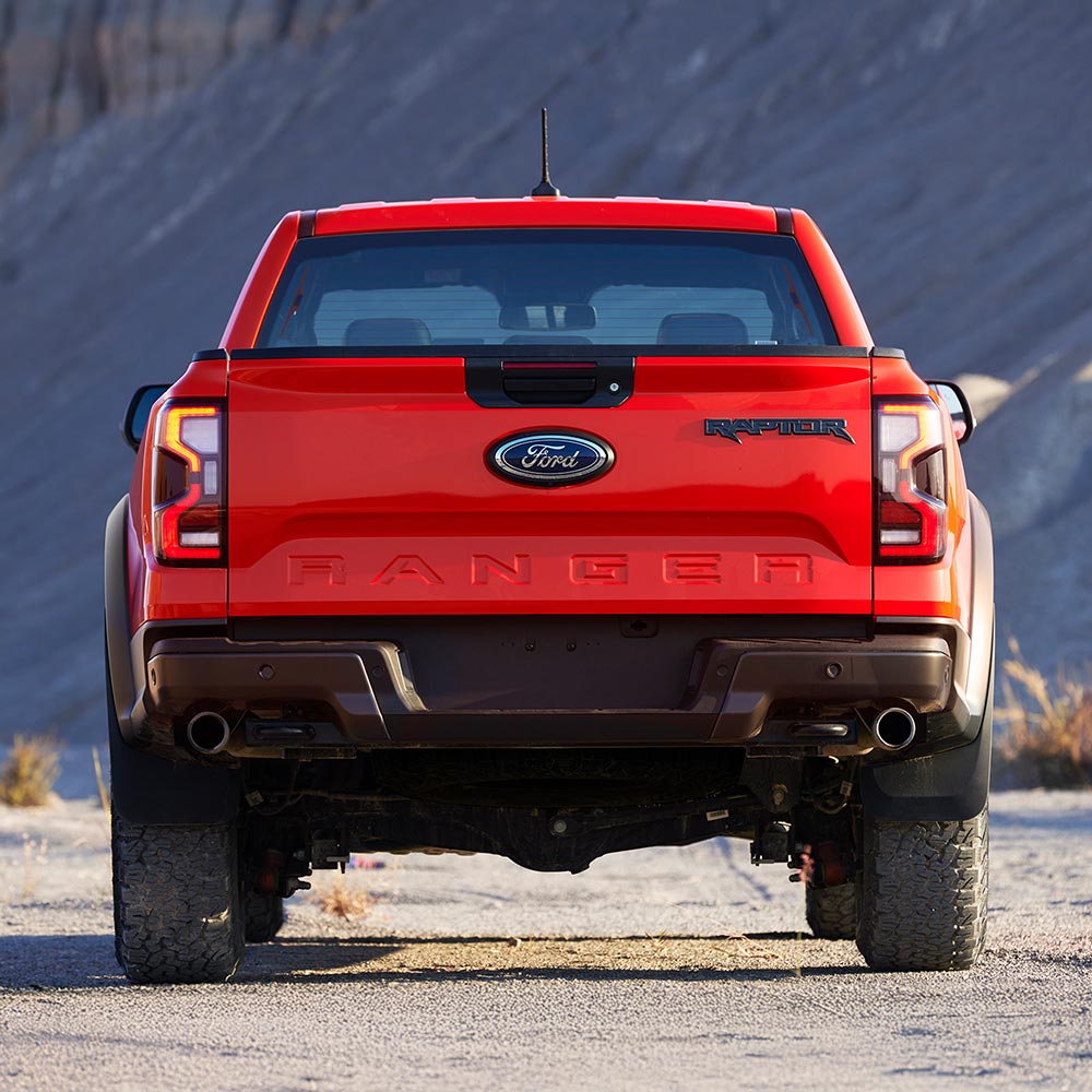 Egy Code Orange színű Ford Ranger Raptor a szabadban parkol, hátulnézetből.