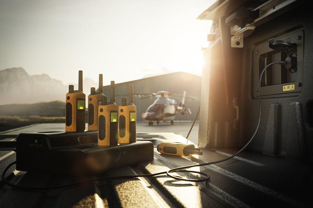 Számos adóvevő töltődik egy Ranger Raptor rakterében naplementekor, a háttérben egy helikoptert látunk.