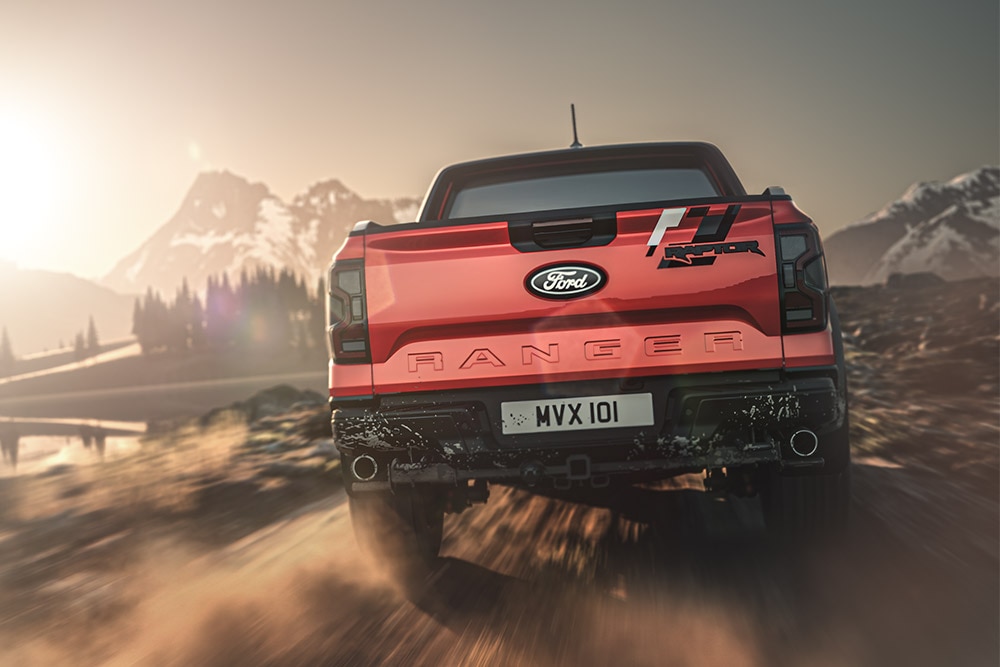 Hátulnézetből látunk egy piros Ford Ranger Raptort, mely földúton halad, a háttérben hegyvidéki tájjal.