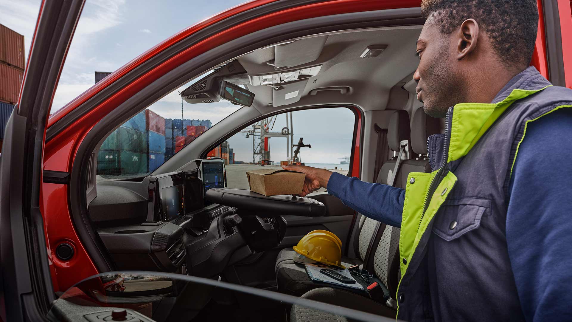 Valaki egy csomagot helyez egy piros Ford Transit Customba.