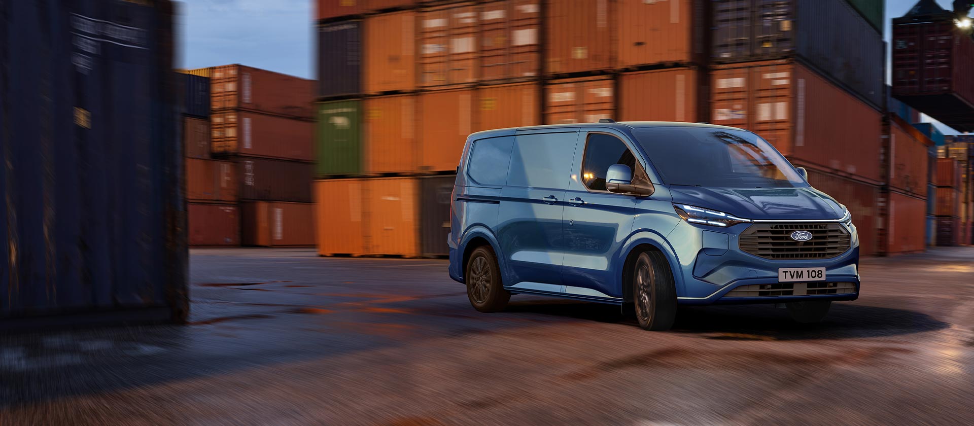 Egy kék Ford Transit Custom plug-in hibrid egy kikötői területen halad át.