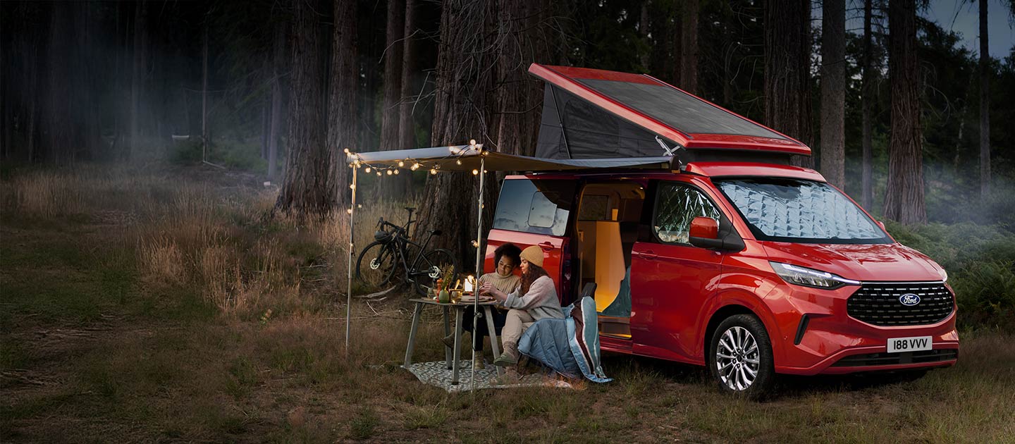 Egy piros Ford Transit Custom Nugget lakóautó egy erdőben parkol.