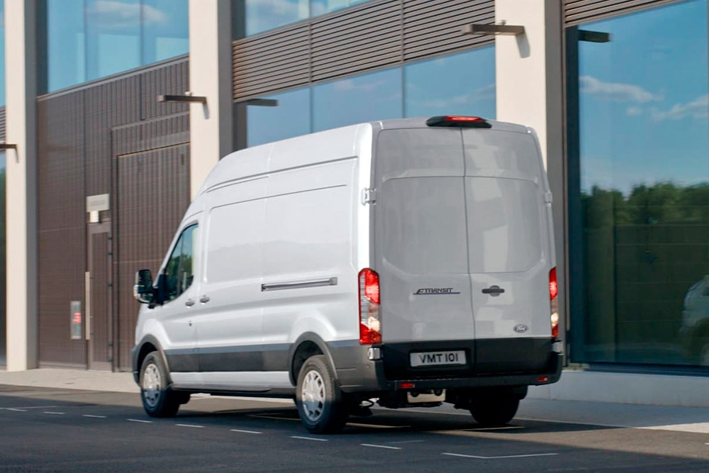 Egy utcán parkoló fehér Ford Transit áruszállító hátulnézetből.