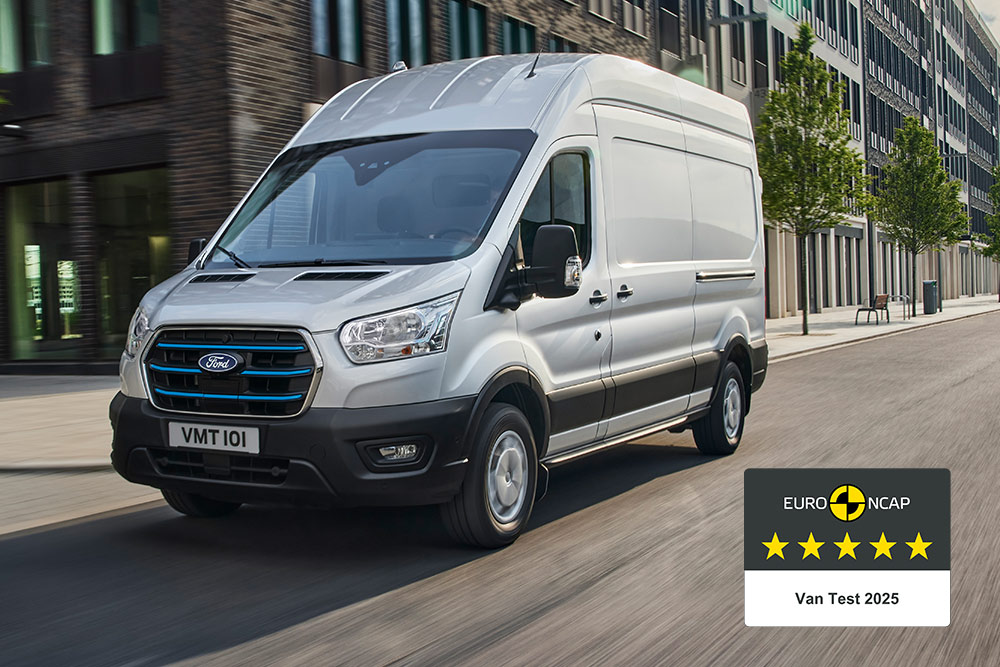 Egy ezüstszínű Ford E-Transit elektromos áruszállító halad az úton, a járművön a „Gold 2022 Commercial Van Safety” jelvény látható.