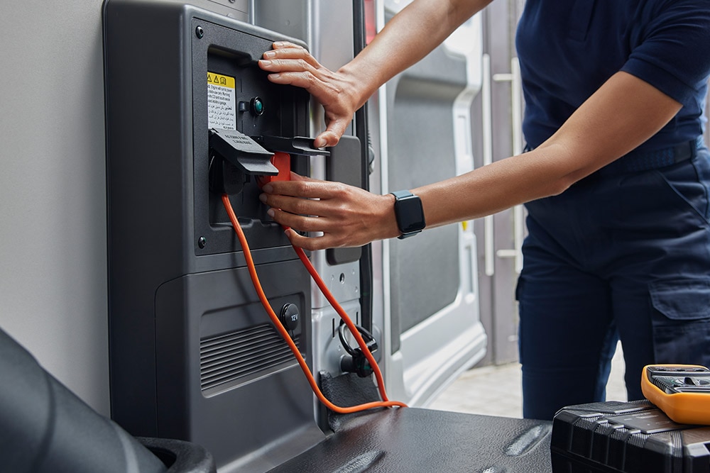 Egy személy egy elektromos töltőkábelt csatlakoztat egy Ford E-Transit elektromos áruszállító belsejében.
