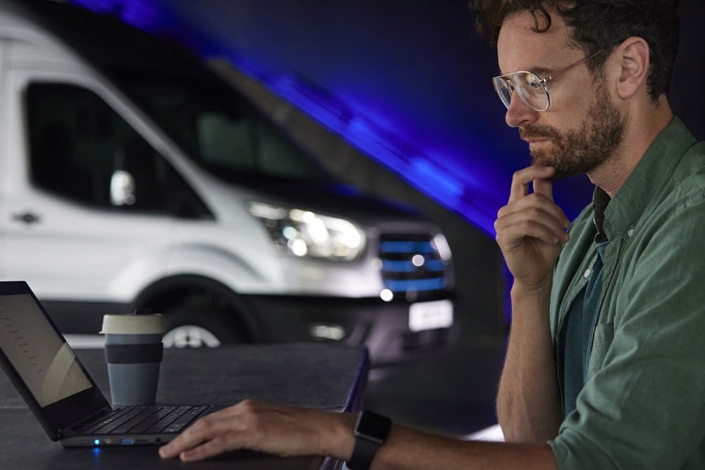 Két szerelő egy garázsban egy Ford E-Transit elektromos áruszállító előtt egy tabletet néz.