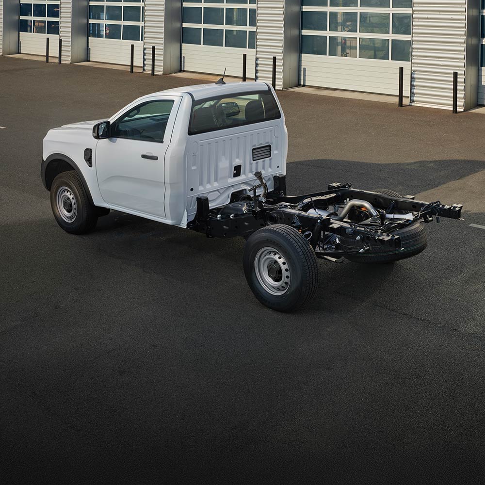 Egy fehér Ford Ranger Fülkés Alváz parkol egy sor garázsajtó előtt.