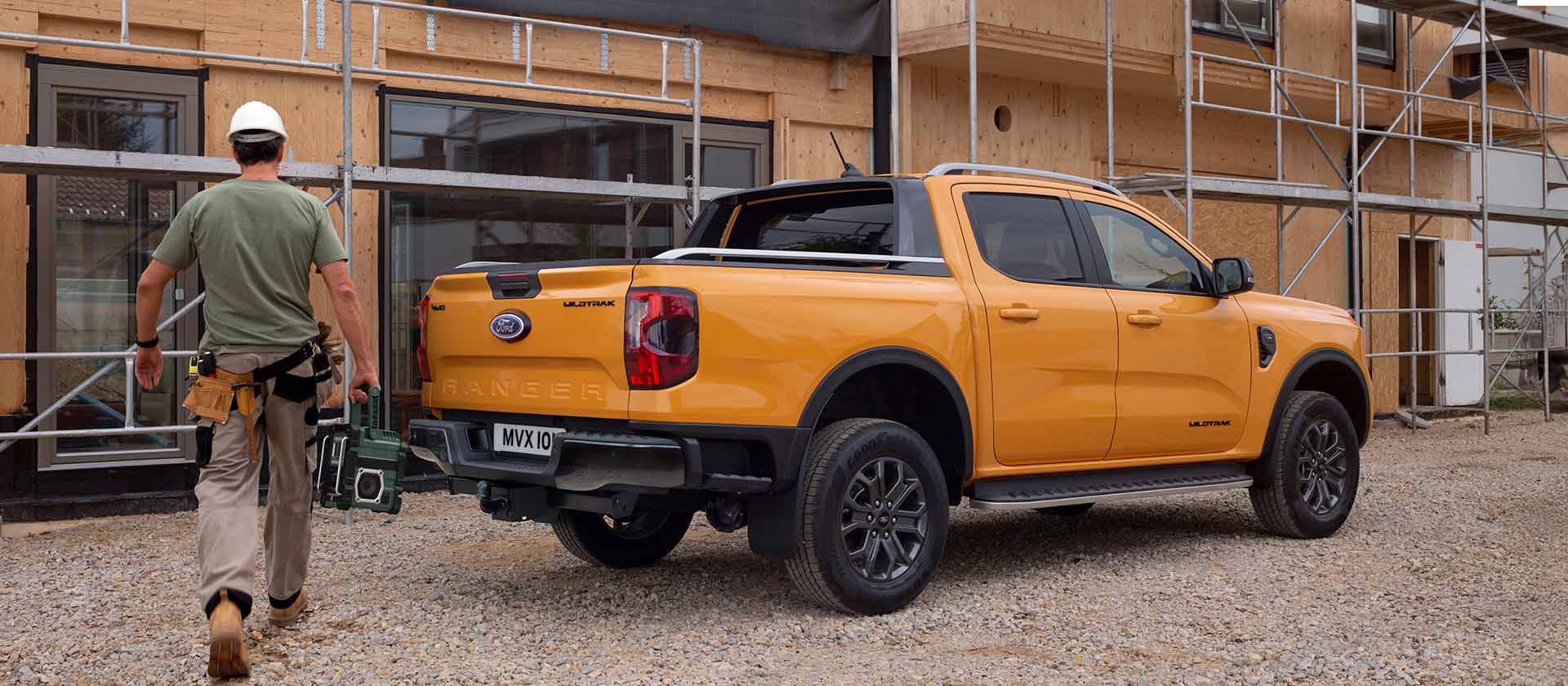 Egy védősisakot viselő munkás egy sárga Ford Ranger pick-up felé sétál egy építkezésen.
