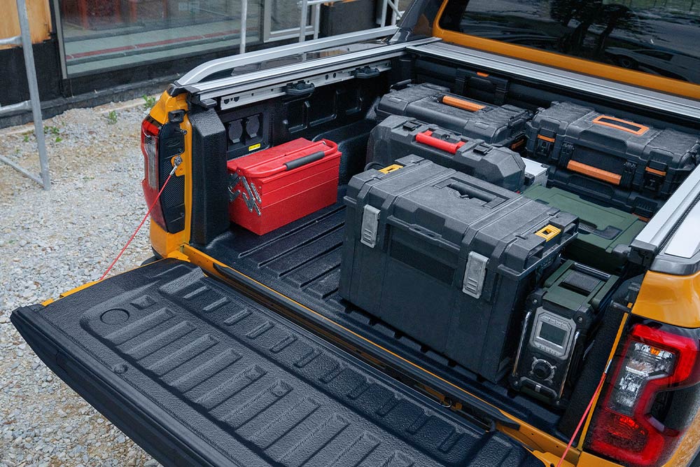 Egy leengedett hátfalú, sárga Ford Rangert látunk, amelyhez szorítóval rögzítettek fadeszkát.