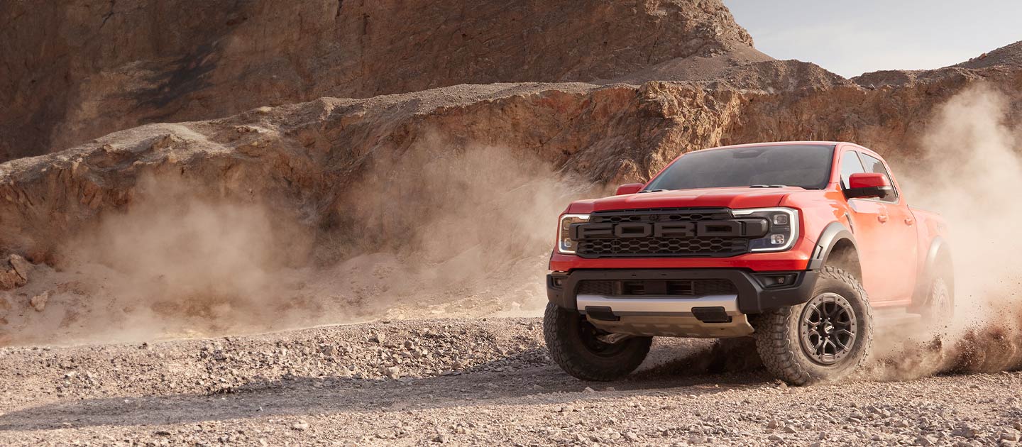 Egy piros Ford Ranger Raptort látunk, ami a sivatagon áthaladva port ver fel maga után.