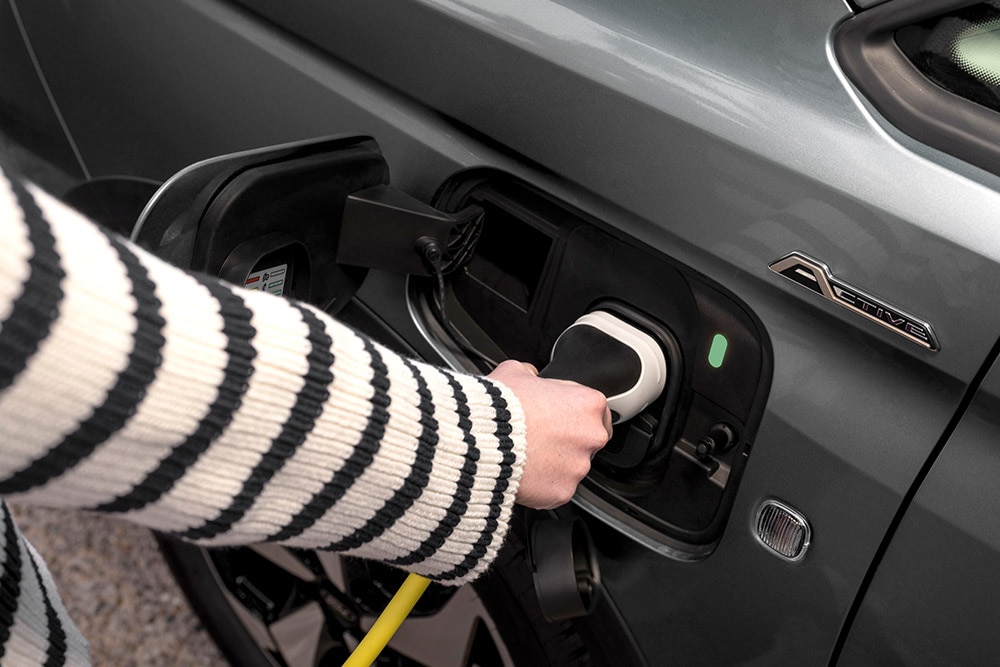 Egy személy egy elektromos töltőkábelt csatlakoztat a Ford Transit Connect plug-in hibrid járműhöz.