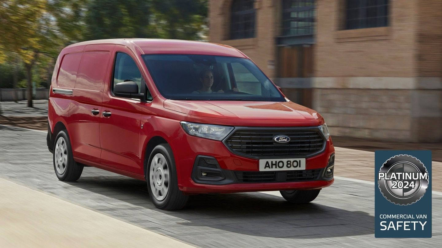 A vadonatúj, Maple Red színű Ford Transit Connect Trend utcán halad, első hűtőrácsát és automatikus fényszóróit látjuk. 