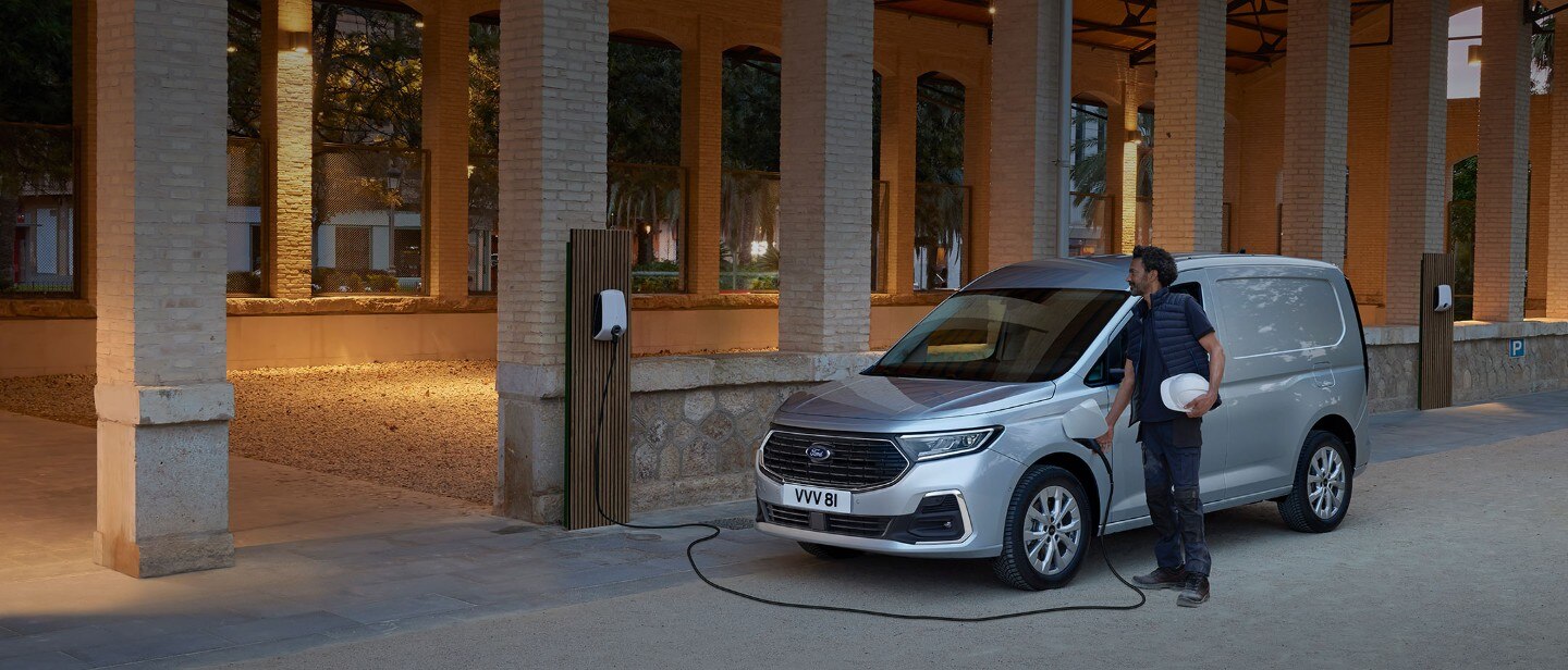 Egy férfi fali töltőkábelt csatlakoztat a vadonatúj, Stardust Silver színű Ford Transit Connecthez.