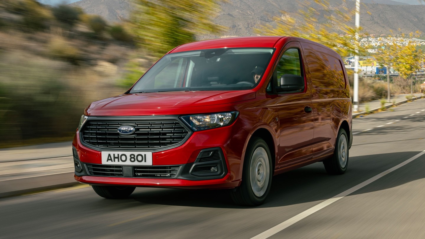 A vadonatúj, Maple Red színű Ford Transit Connect Trend egy úton halad, első hűtőrácsa és fényszórója látszik. 