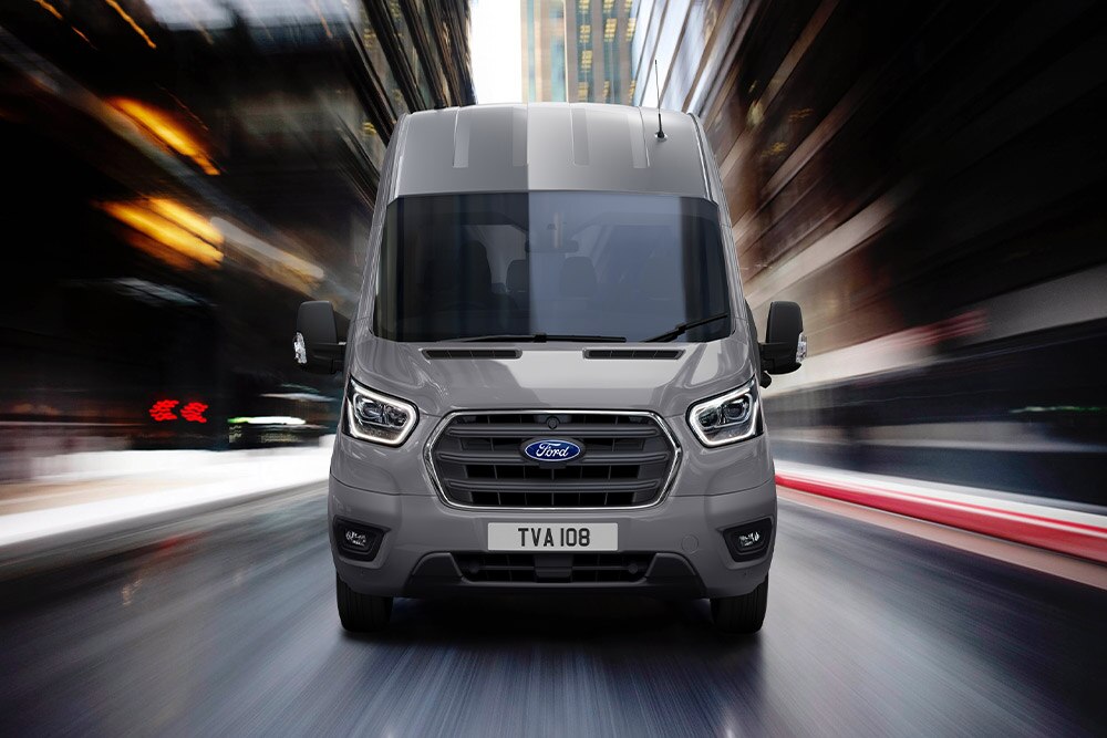 Egy Ford Transit Van egy városban halad az úton, elölnézetből.
