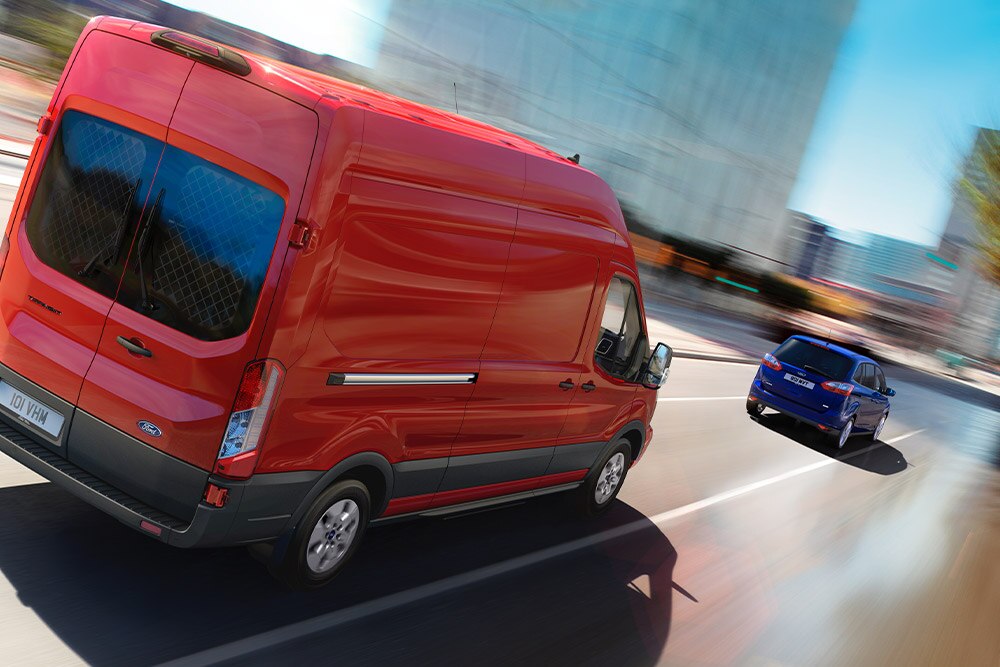 Egy piros Ford Transit halad egy úton.