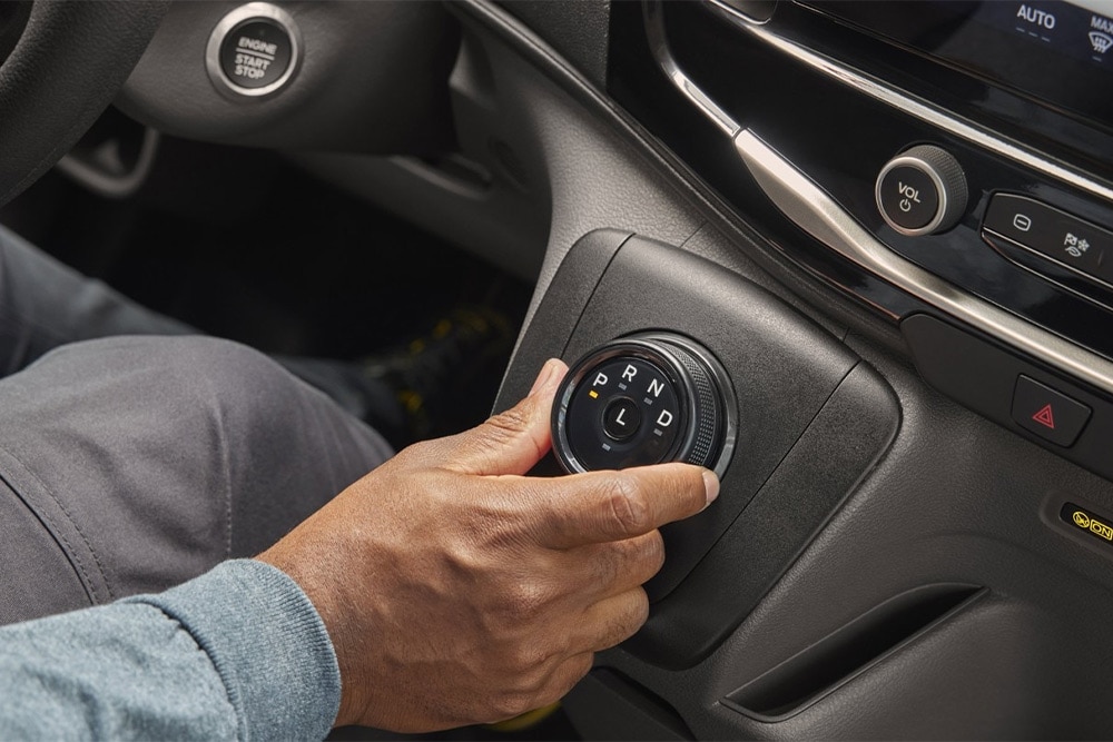 Egy kéz egy Ford Transit Van középkonzolján elhelyezett sebességváltó tárcsát kezeli.