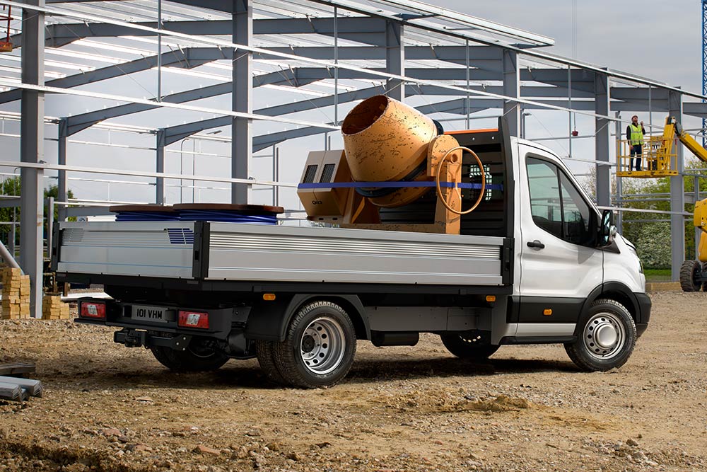 A Ford Transit alváz cementkeverővel a platóján építési területen parkol.