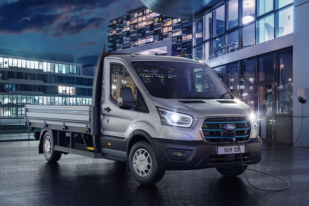Ezüstszínű Ford Transit fülkés alváz parkol éjszaka egy modern épület előtt.