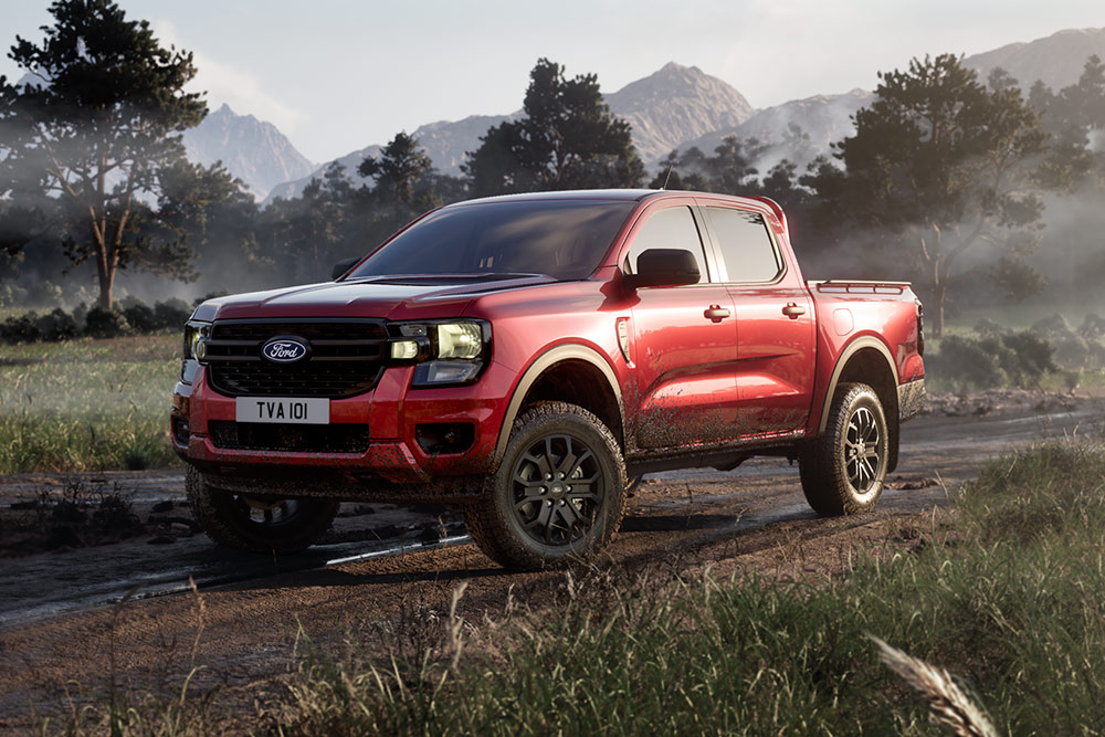 Egy piros Ford Ranger Raptor festői tájon átvezető földúton halad.