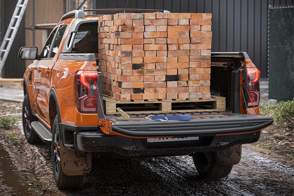 Egy narancsszínű Ford Ranger hátsó részét látjuk, a platójára téglát pakolnak.