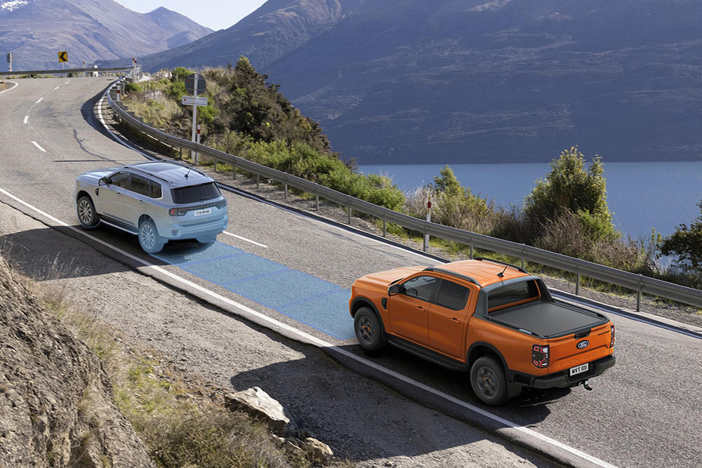 Egy továbbfejlesztett vezetéstámogató rendszert használó narancsszínű Ford Ranger halad egy tengerparti autópálya mentén. 