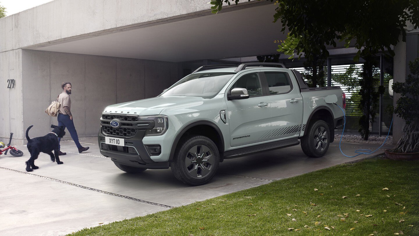 Kutyát sétáltató férfi bemegy egy modern házba, közben elhalad parkoló Ford Ranger Stormtrak Plug-in Hybrid mellett. 
