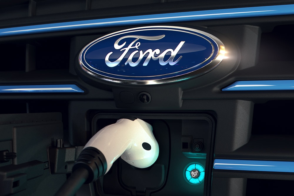 Közelképen látunk egy fehér töltőkábelt, mely egy Ford elektromos jármű első töltőportjába van csatlakoztatva.