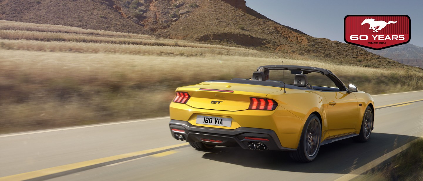 Yellow Ford Mustang riding a road rear view
