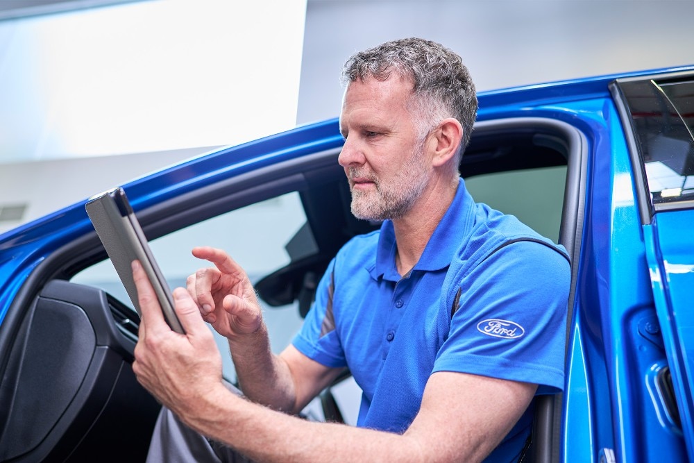 Egy Ford technikus ül egy kék Ford járműben, és táblagéppel ellenőrzi a jármű rendszereit. 